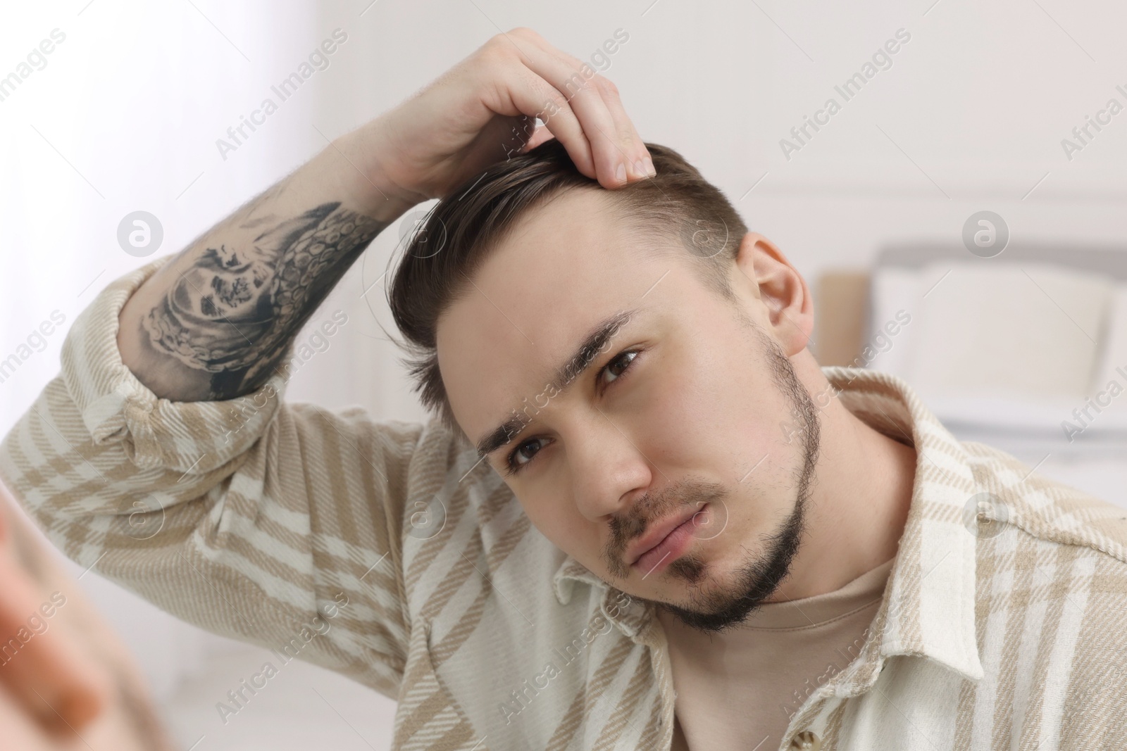 Photo of Baldness concept. Sad man with receding hairline looking at mirror indoors