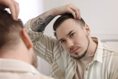 Photo of Baldness concept. Sad man with receding hairline looking at mirror indoors