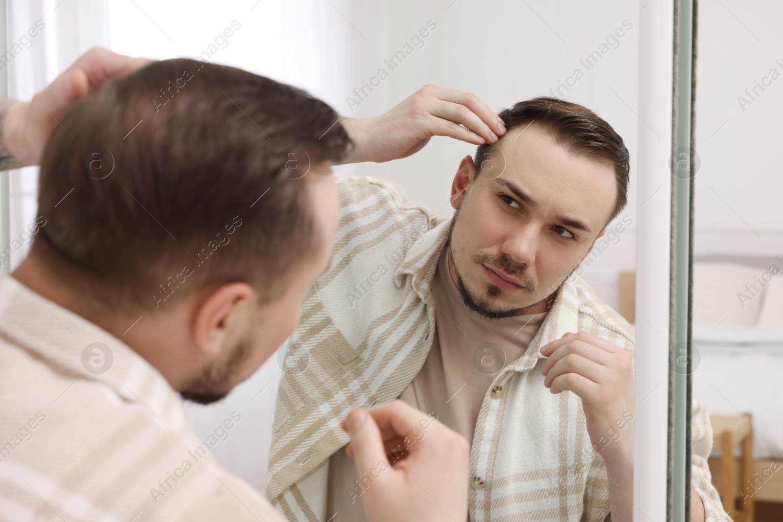 Photo of Baldness concept. Sad man with receding hairline looking at mirror indoors