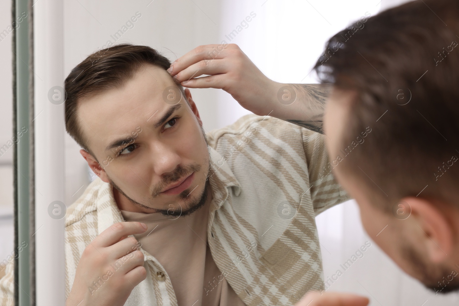 Photo of Baldness concept. Sad man with receding hairline looking at mirror indoors