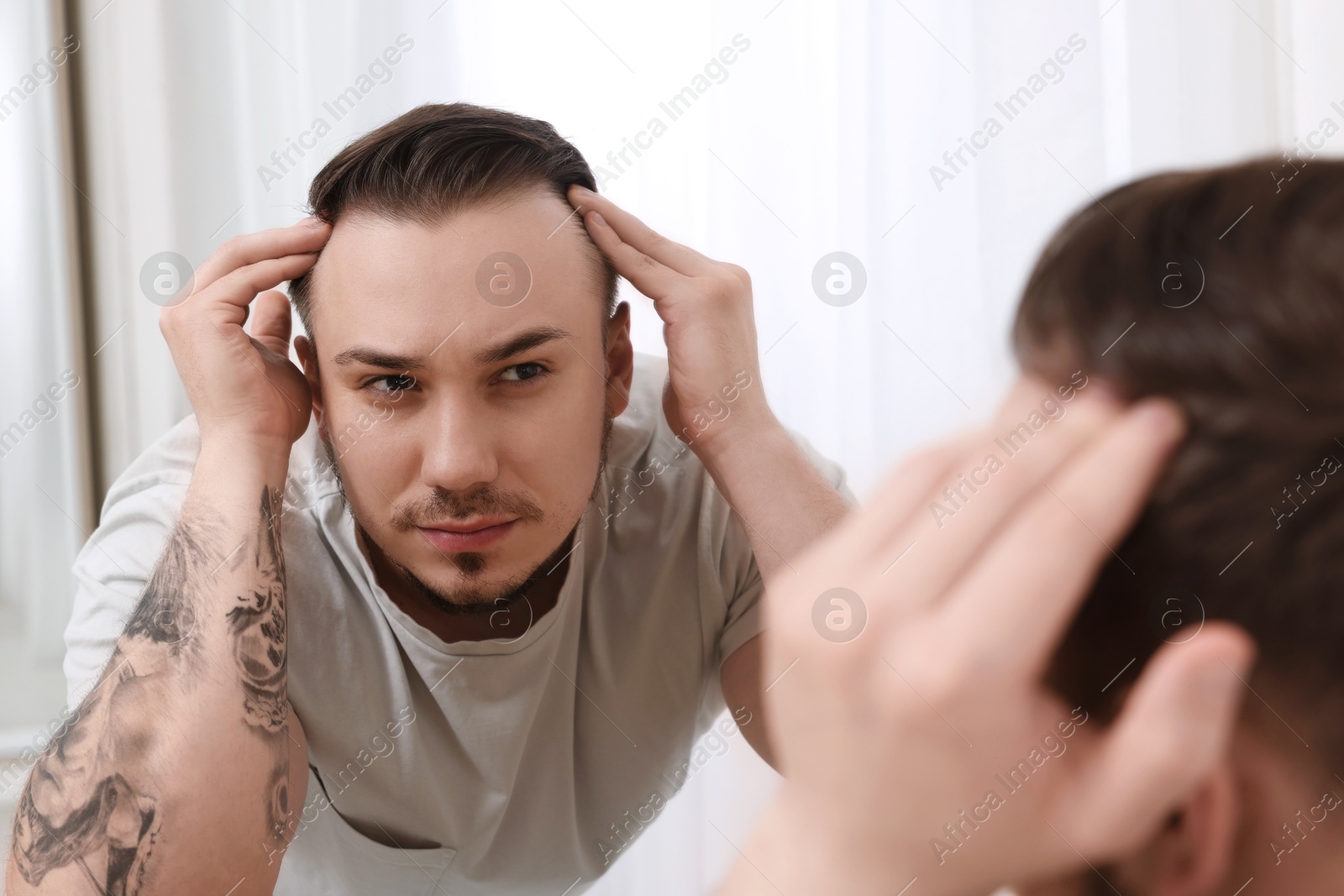 Photo of Baldness concept. Sad man with receding hairline looking at mirror indoors