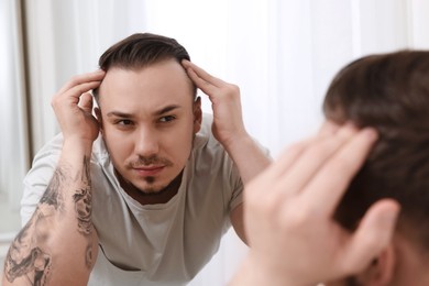 Photo of Baldness concept. Sad man with receding hairline looking at mirror indoors