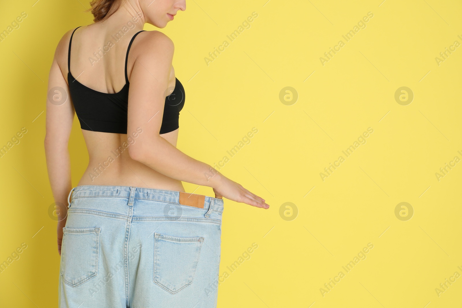 Photo of Woman in big jeans showing her slim body on yellow background, closeup. Space for text