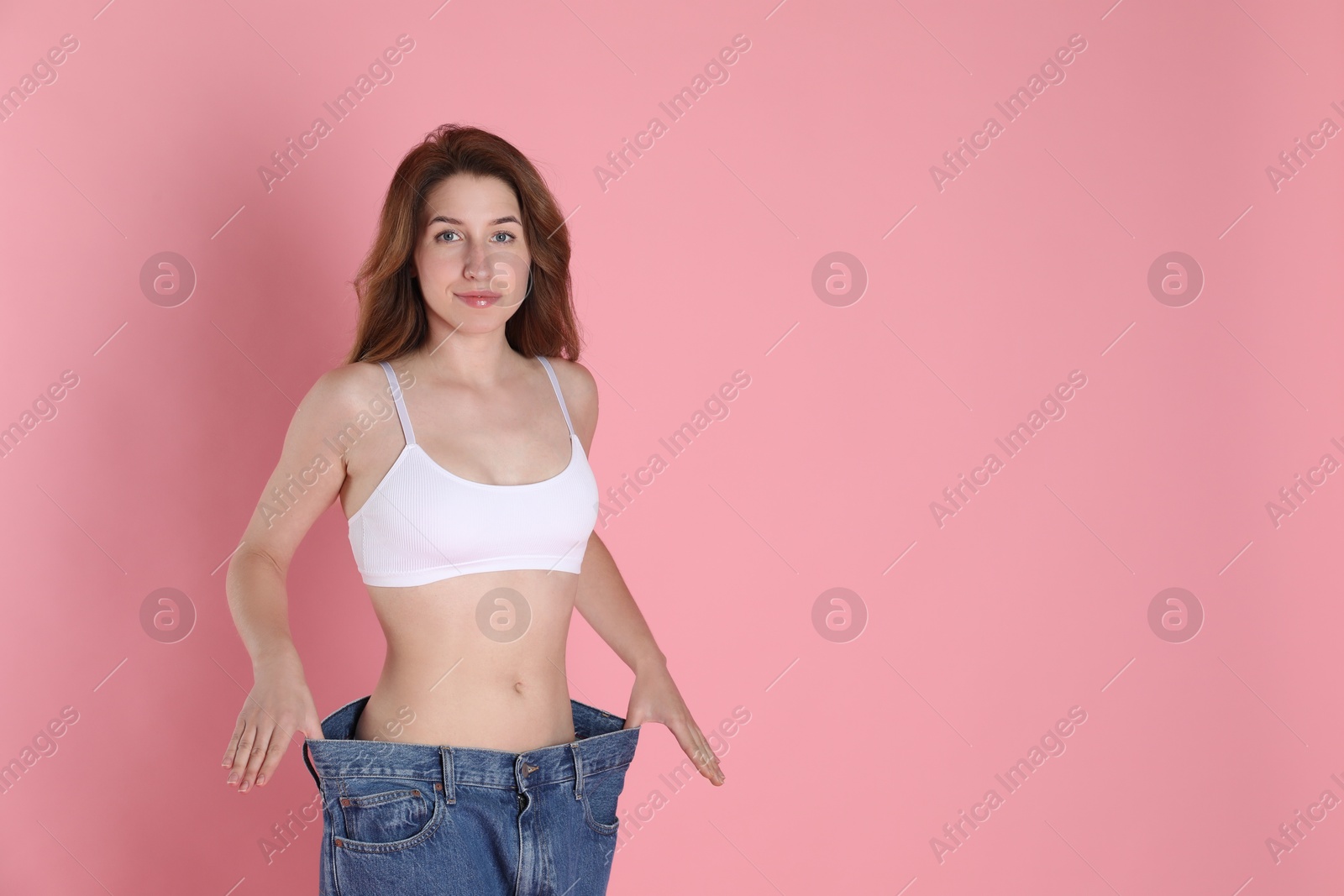 Photo of Woman in big jeans showing her slim body on pink background, space for text