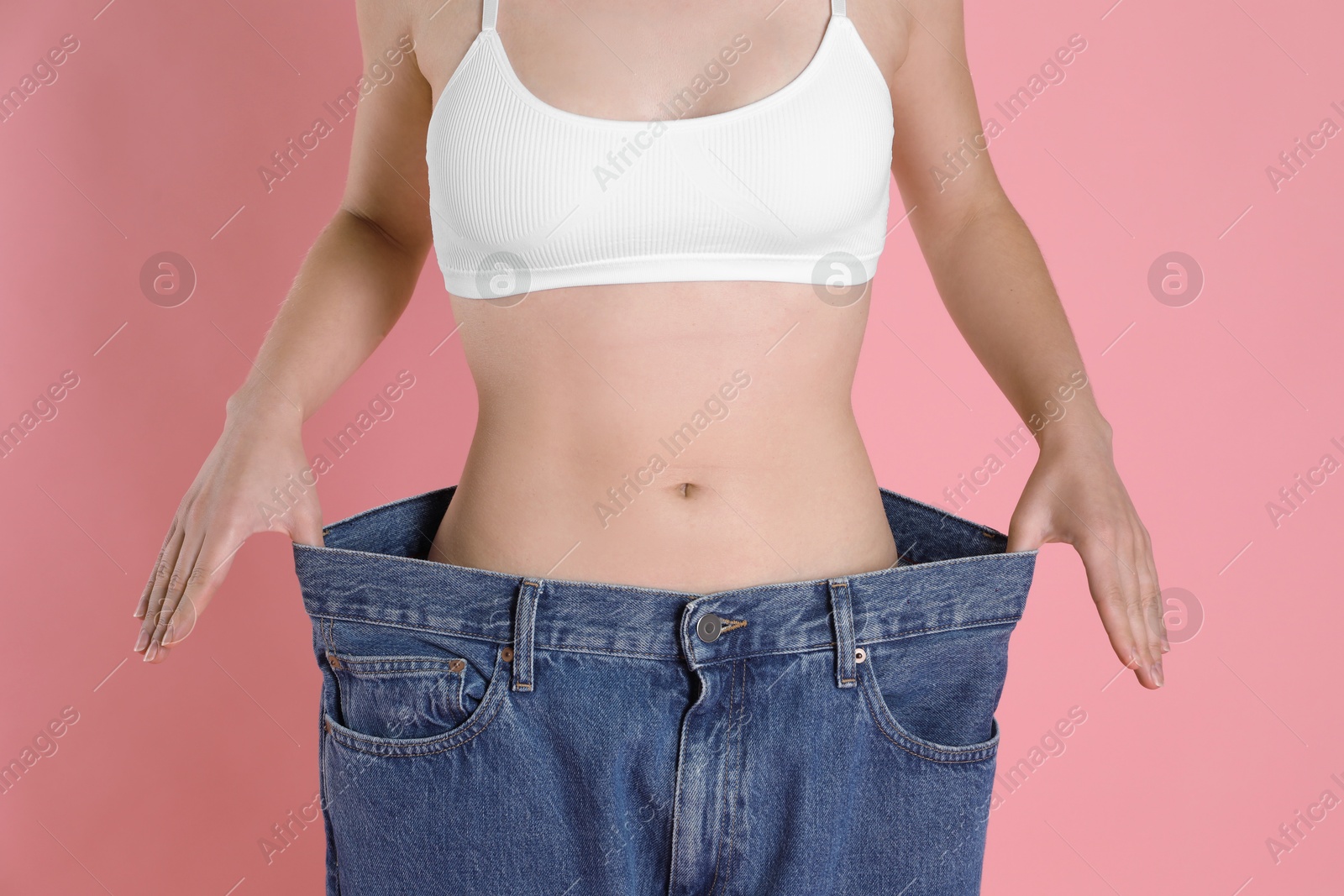 Photo of Woman in big jeans showing her slim body on pink background, closeup