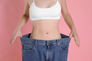 Photo of Woman in big jeans showing her slim body on pink background, closeup