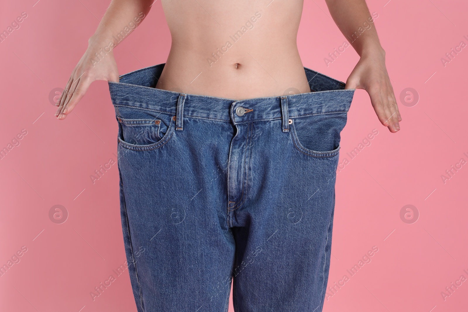 Photo of Woman in big jeans showing her slim body on pink background, closeup