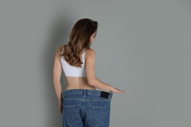 Woman in big jeans showing her slim body on grey background. Space for text