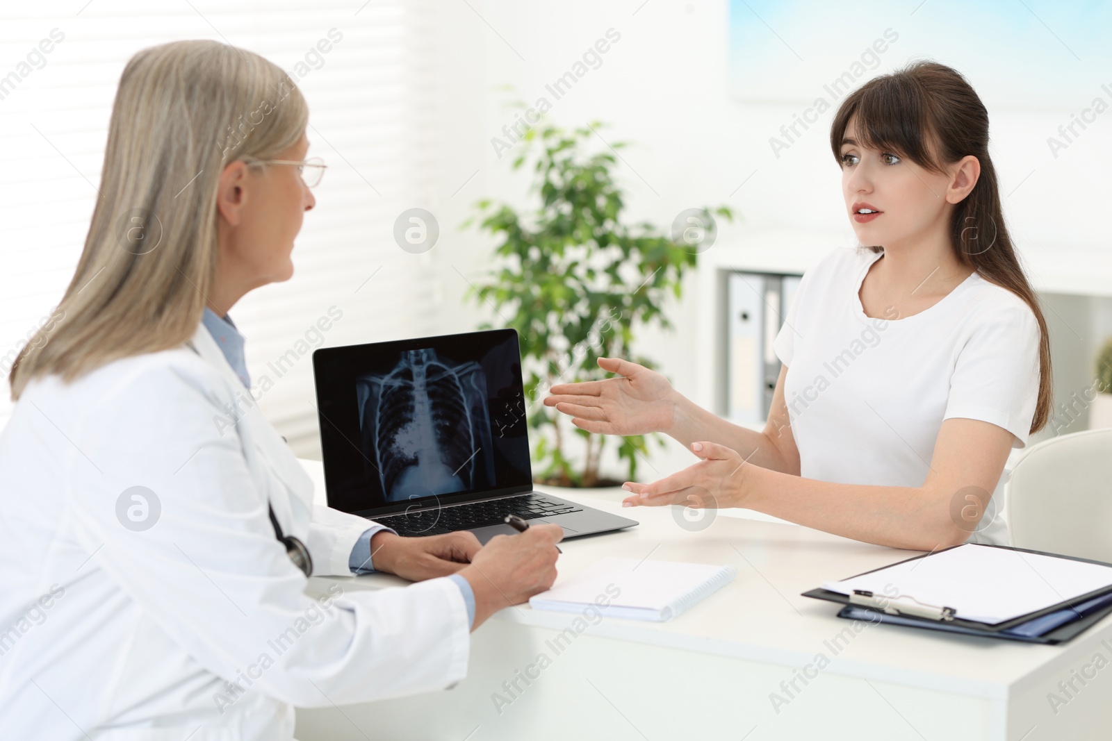 Photo of Lung cancer. Doctor showing chest x-ray on laptop to her patient in clinic