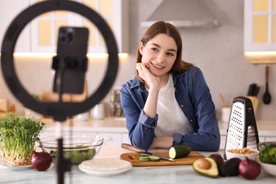 Food blogger cooking while recording video with smartphone and ring lamp in kitchen