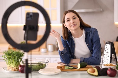 Food blogger cooking while recording video with smartphone and ring lamp in kitchen