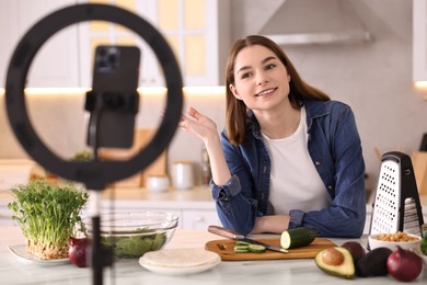 Photo of Food blogger cooking while recording video with smartphone and ring lamp in kitchen