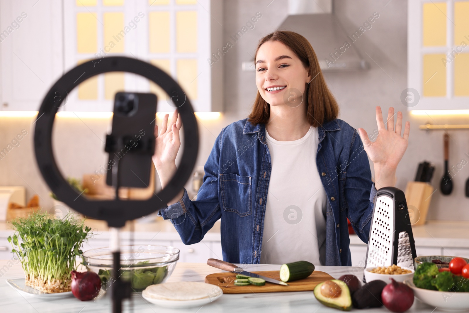 Photo of Food blogger cooking while recording video with smartphone and ring lamp in kitchen