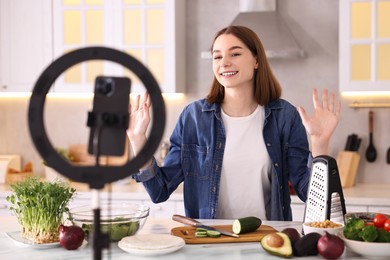 Food blogger cooking while recording video with smartphone and ring lamp in kitchen