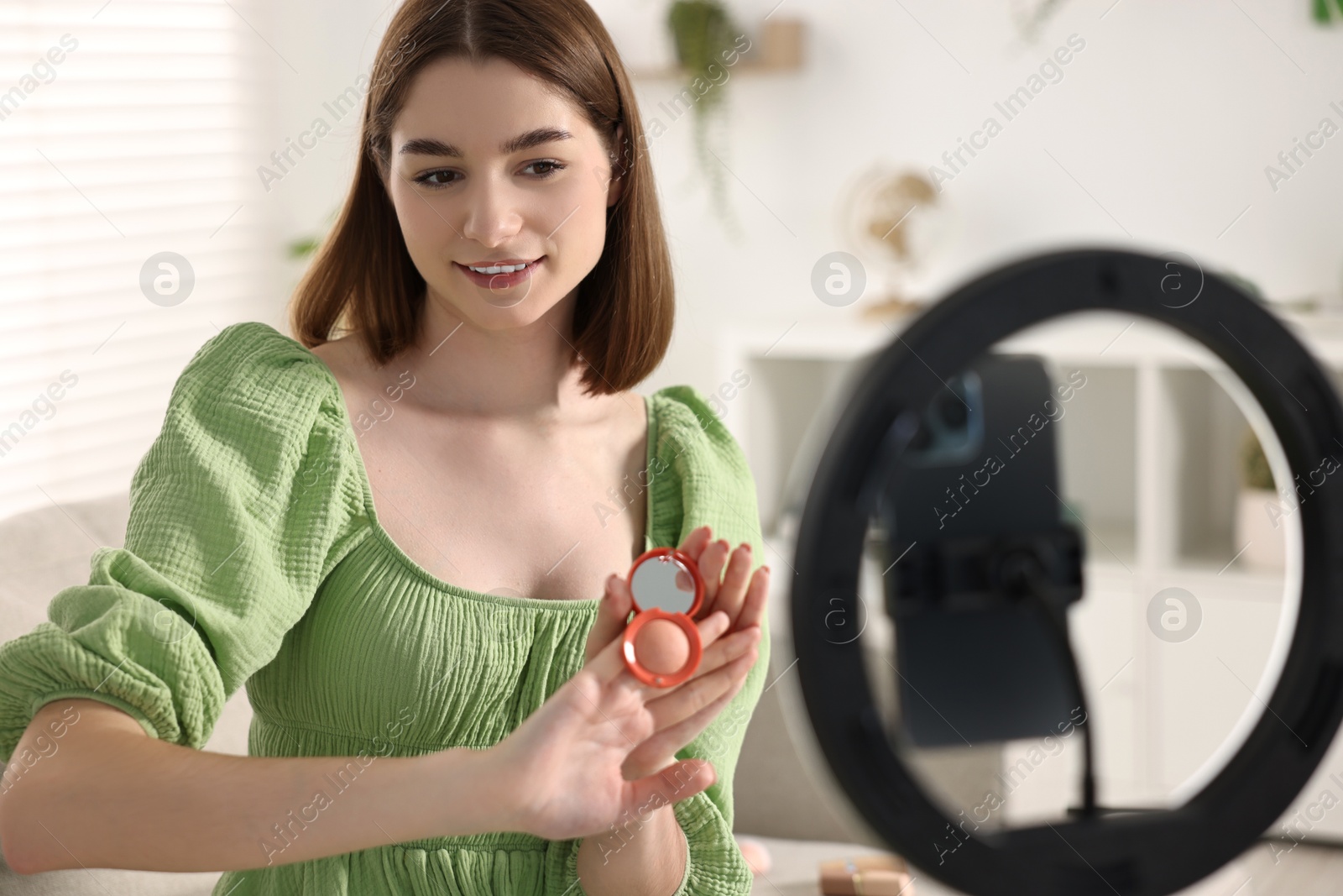 Photo of Beauty blogger reviewing decorative cosmetic products and recording video with smartphone and ring lamp at home