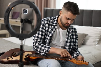 Photo of Music blogger recording guitar lesson with smartphone and ring lamp at home