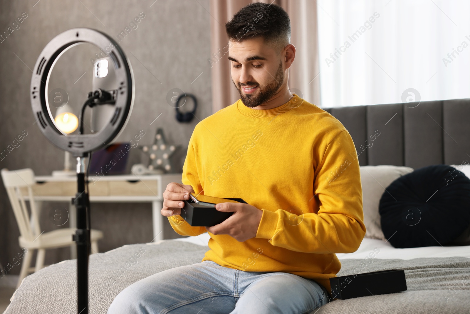 Photo of Technology blogger reviewing phone and recording video with smartphone and ring lamp at home