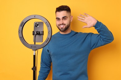 Blogger recording video with smartphone and ring lamp on orange background