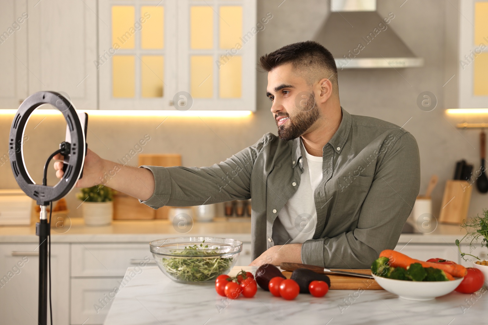 Photo of Food blogger cooking while recording video with smartphone and ring lamp in kitchen