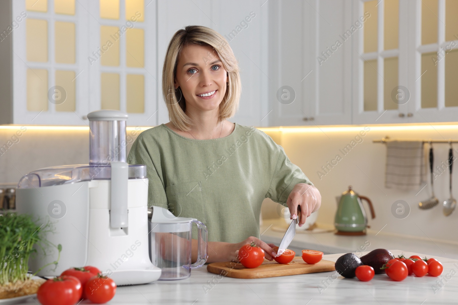 Photo of Juicer and fresh products on white marble table. Smiling woman cutting tomato in kitchen