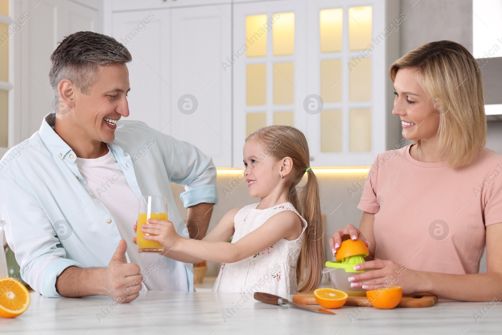 Photo of Happy family with juicer and fresh products making juice at white marble table in kitchen