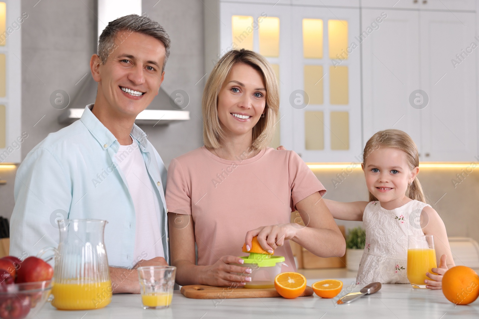 Photo of Happy family with juicer and fresh products making juice at white marble table in kitchen