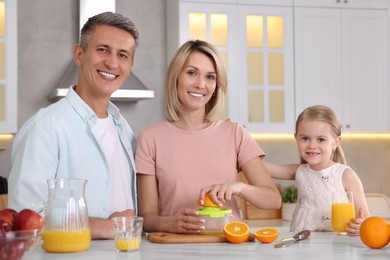 Photo of Happy family with juicer and fresh products making juice at white marble table in kitchen