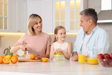 Photo of Happy family making juice at white marble table in kitchen