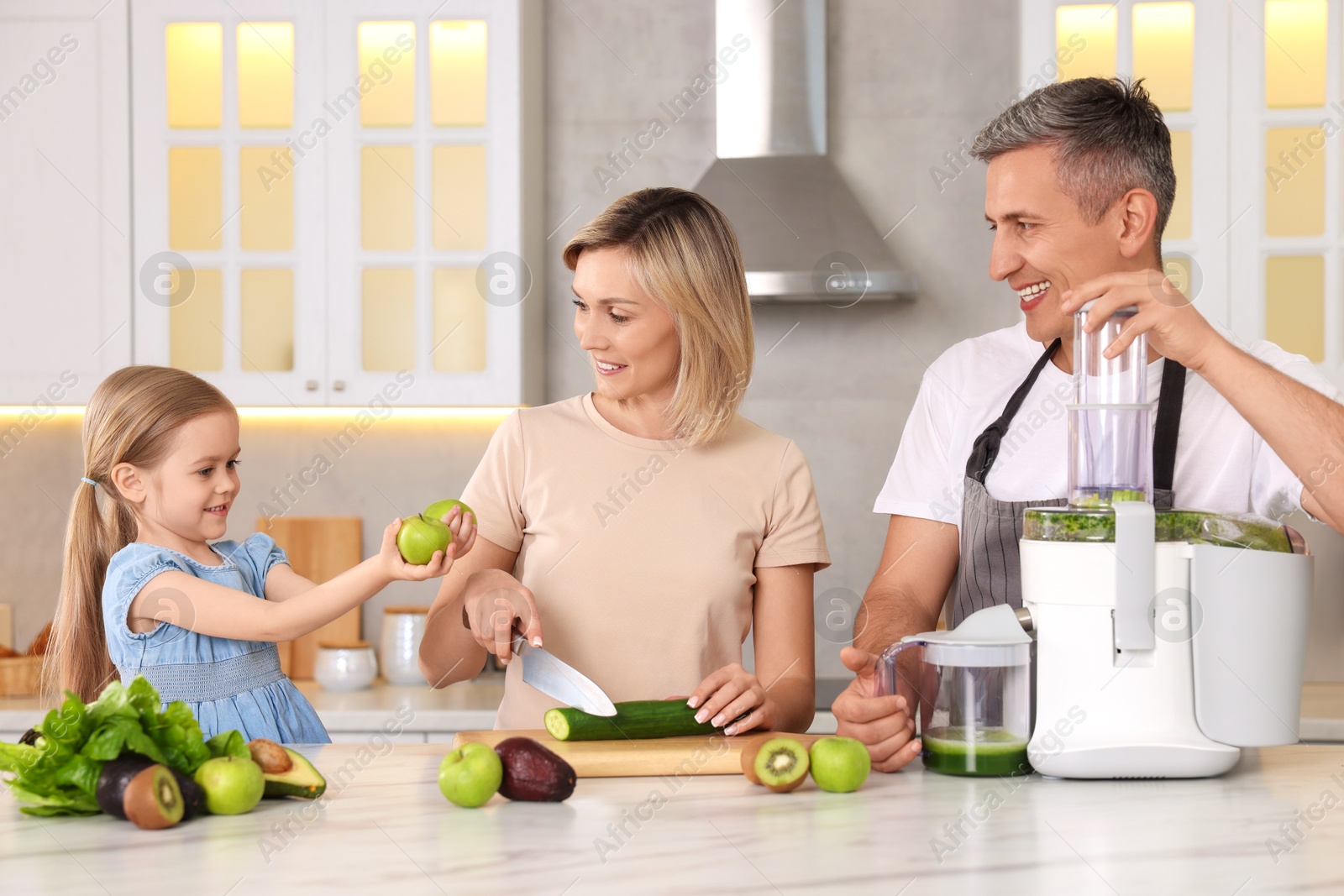 Photo of Happy family with juicer and fresh products making drink at white marble table in kitchen