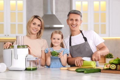 Happy family with juicer and fresh products making drink at white marble table in kitchen