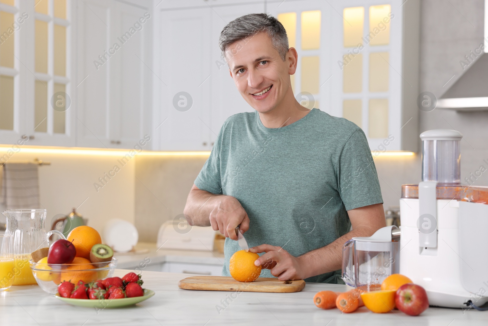 Photo of Juicer and fresh products on white marble table. Smiling man cutting orange in kitchen