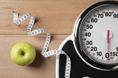 Photo of Scale, measuring tape and fresh apple on wooden floor, flat lay