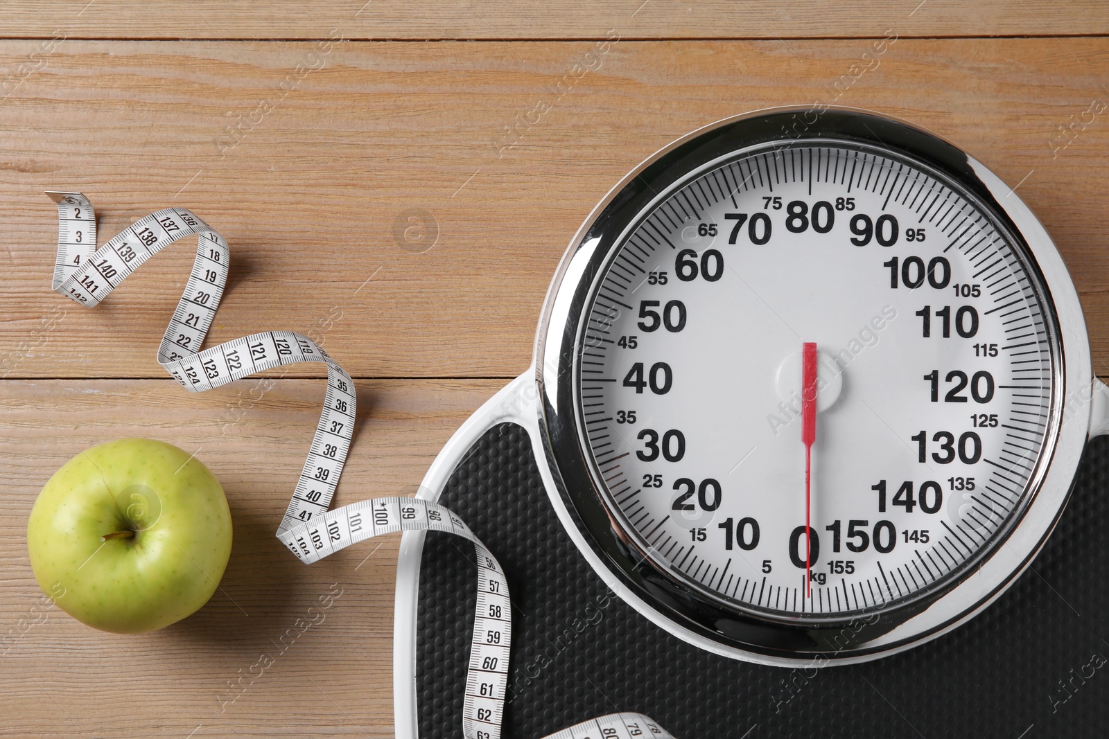 Photo of Scale, measuring tape and fresh apple on wooden floor, flat lay