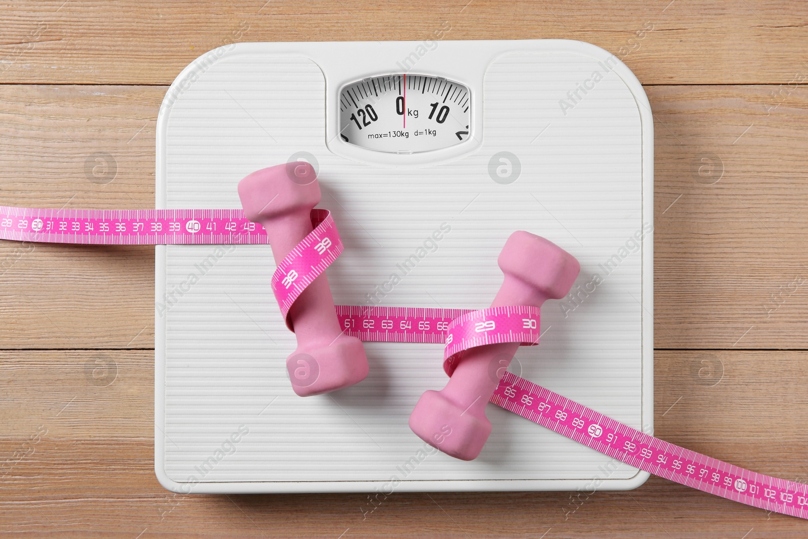 Photo of Scale, measuring tape and dumbbells on wooden floor, top view