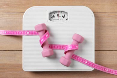 Photo of Scale, measuring tape and dumbbells on wooden floor, top view