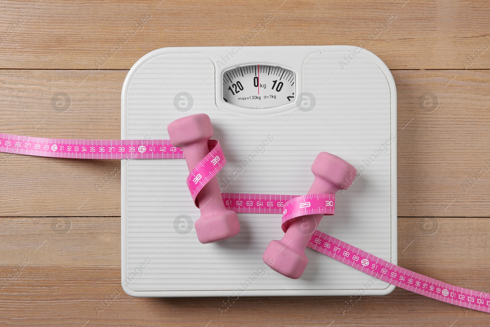 Photo of Scale, measuring tape and dumbbells on wooden floor, top view