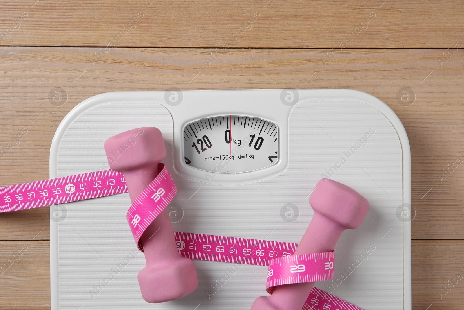 Photo of Scale, measuring tape and dumbbells on wooden floor, top view