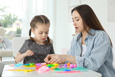 Mother and her daughter sculpting with play dough at table indoors