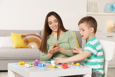 Smiling mother and her son sculpting with play dough at table indoors