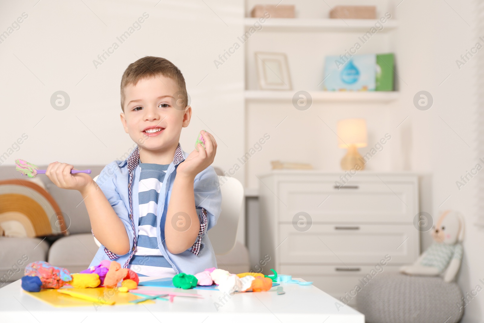 Photo of Smiling boy sculpting with play dough at table in kindergarten. Space for text