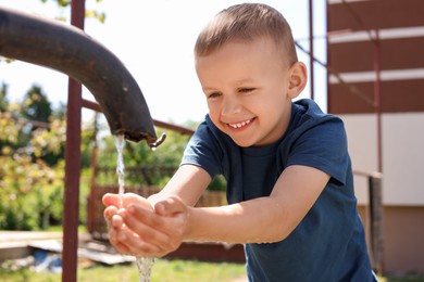 Water scarcity. Cute little boy drawing water with hands from tap outdoors