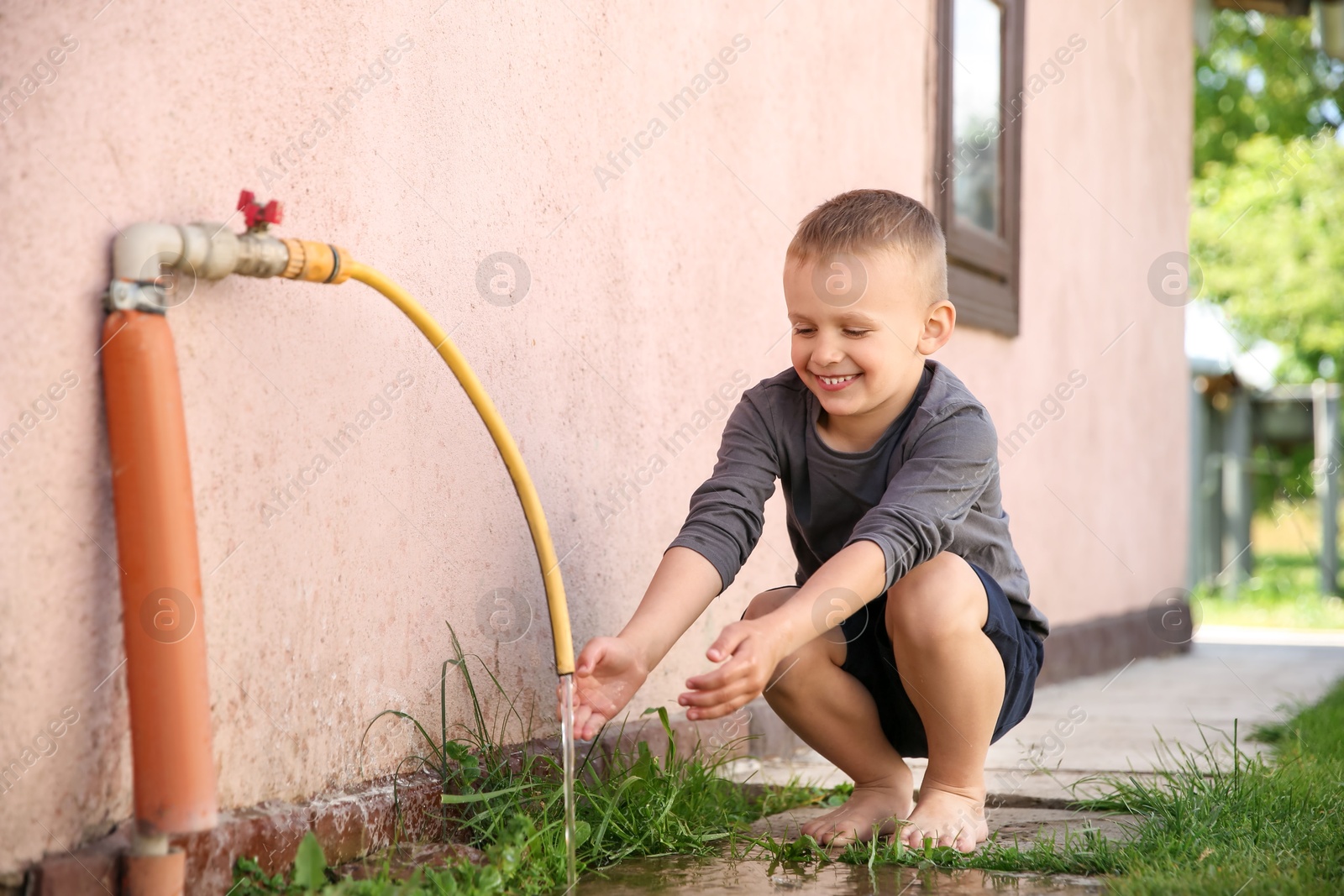 Photo of Water scarcity. Cute little boy drawing water with hands from tap outdoors