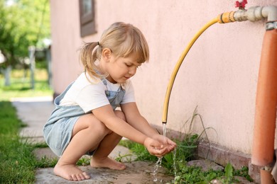 Water scarcity. Cute little girl drawing water with hands from tap outdoors