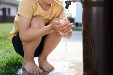 Water scarcity. Little boy drinking water from tap outdoors, closeup