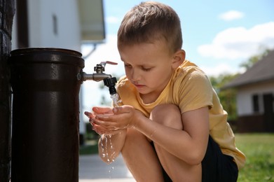 Photo of Water scarcity. Cute little boy drawing water with hands from tap outdoors