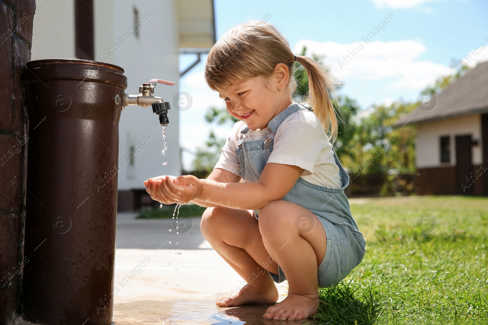 Photo of Water scarcity. Cute little girl drawing water with hands from tap outdoors