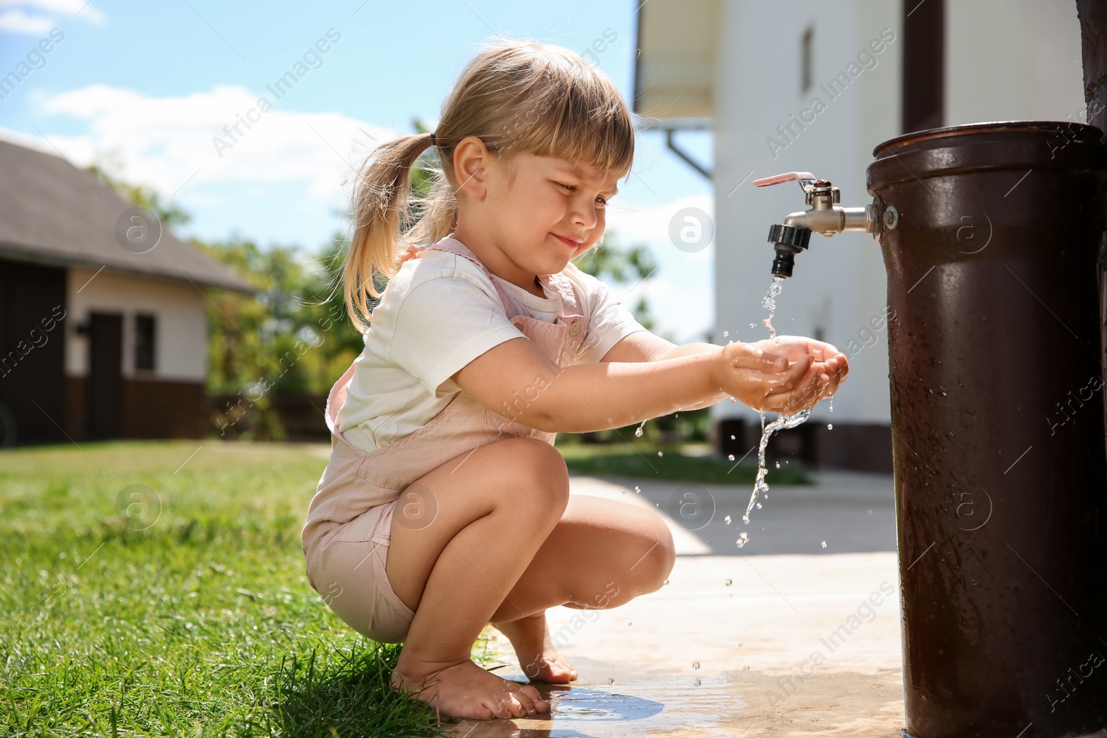 Photo of Water scarcity. Cute little girl drawing water with hands from tap outdoors