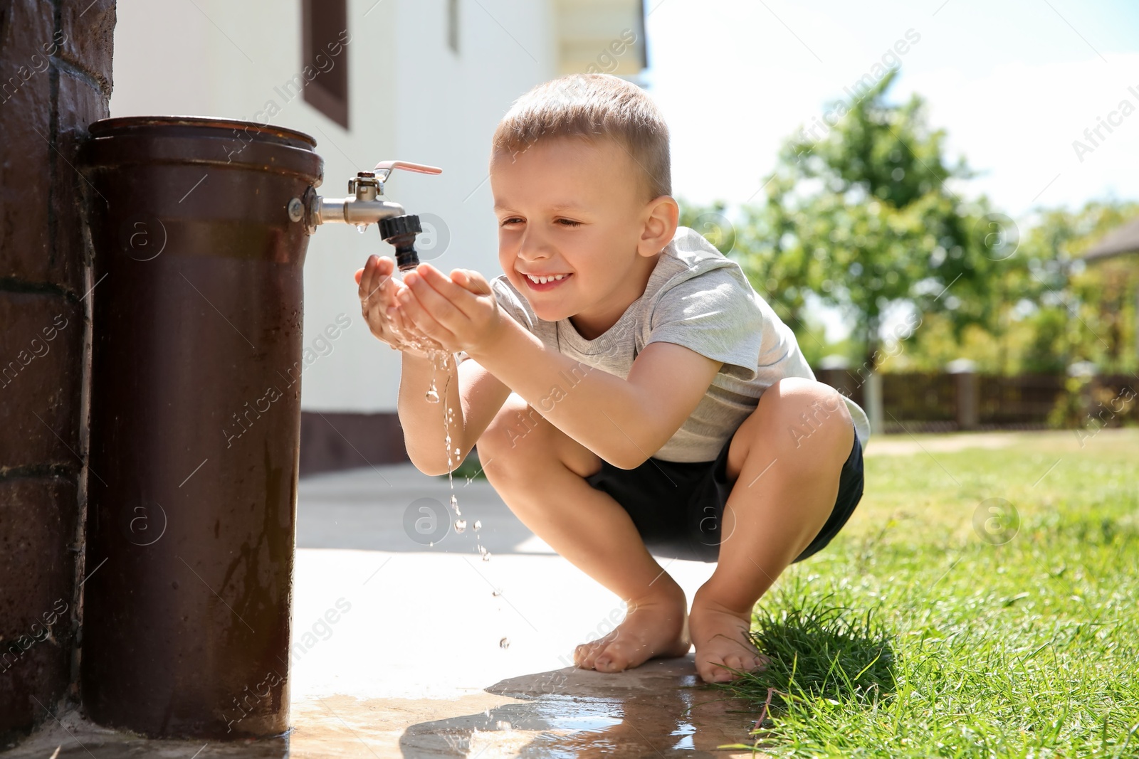 Photo of Water scarcity. Cute little boy drinking water from tap outdoors, space for text