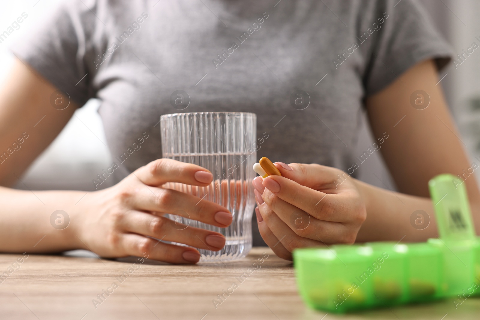 Photo of Woman with pills, organizer and glass of water at wooden table, closeup