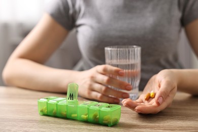 Photo of Woman with pills, organizer and glass of water at wooden table, closeup